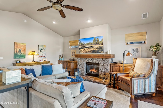 living room featuring hardwood / wood-style flooring, ceiling fan, lofted ceiling, and a stone fireplace