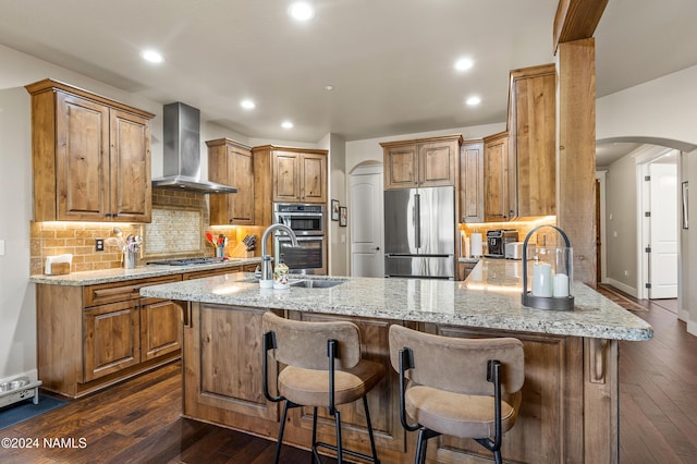 kitchen featuring wall chimney exhaust hood, a kitchen bar, decorative backsplash, and appliances with stainless steel finishes