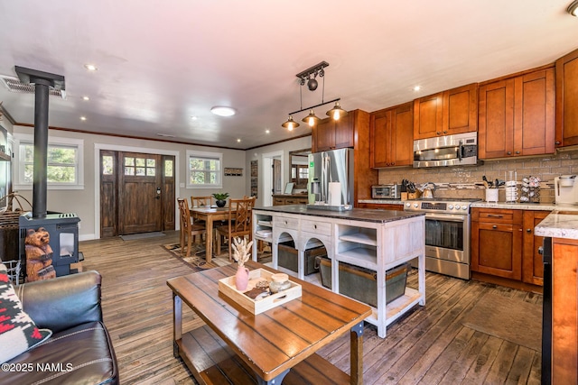 kitchen featuring appliances with stainless steel finishes, backsplash, dark wood finished floors, a wood stove, and crown molding