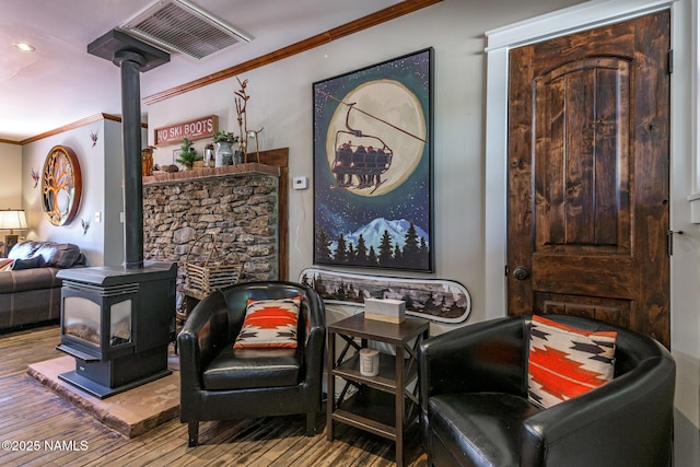 living area with a wood stove, hardwood / wood-style floors, visible vents, and crown molding