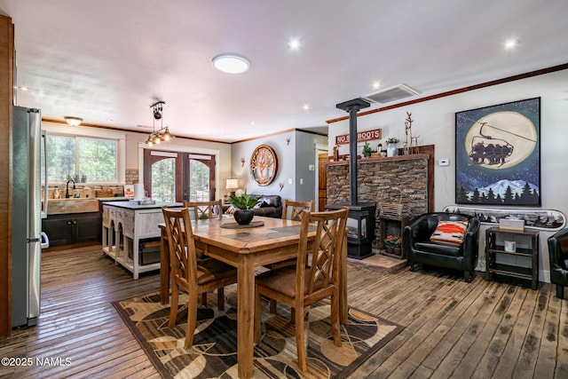 dining area featuring a wood stove, dark wood-style floors, crown molding, and french doors