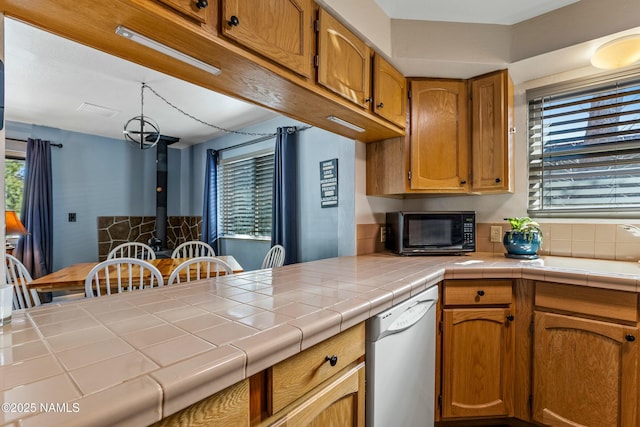 kitchen featuring brown cabinets, a sink, tile countertops, black microwave, and dishwasher