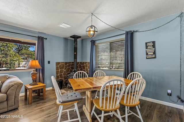 dining space featuring a textured ceiling, wood finished floors, and a wood stove