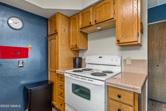 kitchen featuring brown cabinets, white electric stove, a textured wall, and tile counters