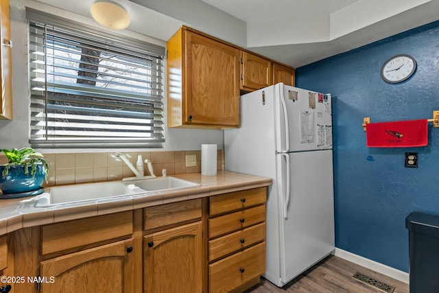 kitchen with visible vents, a sink, wood finished floors, freestanding refrigerator, and baseboards