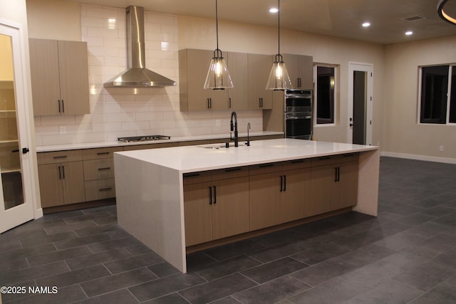 kitchen featuring sink, backsplash, stainless steel appliances, a center island with sink, and wall chimney exhaust hood