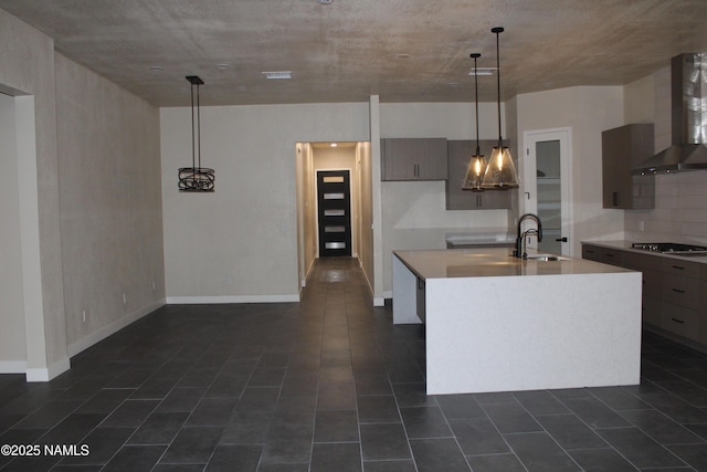 kitchen featuring wall chimney exhaust hood, sink, a center island with sink, pendant lighting, and black gas stovetop