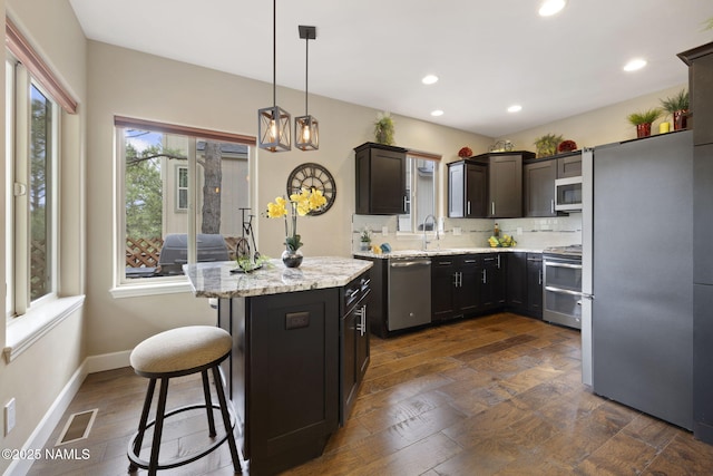 1248 W Lil Ben Trl, Flagstaff, AZ 86001 - kitchen featuring appliances with stainless steel finishes, a center island, a kitchen bar, decorative light fixtures, and light stone counters