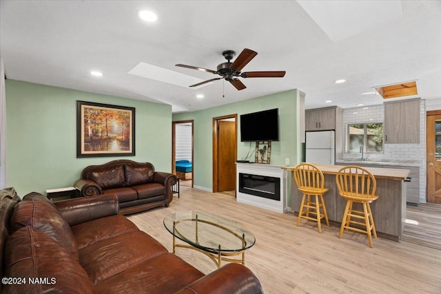 living room with a skylight, light hardwood / wood-style floors, sink, a large fireplace, and ceiling fan