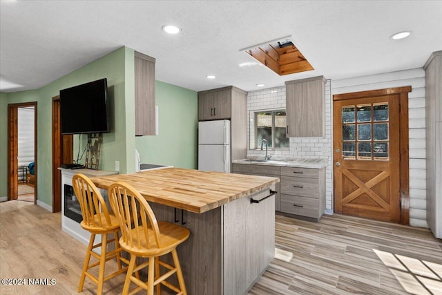 kitchen featuring decorative backsplash, sink, light wood-type flooring, a breakfast bar, and white refrigerator