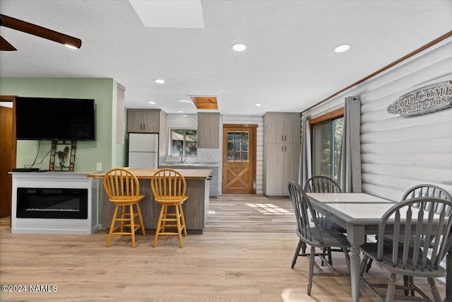 kitchen featuring white refrigerator, light hardwood / wood-style floors, a breakfast bar area, and decorative backsplash