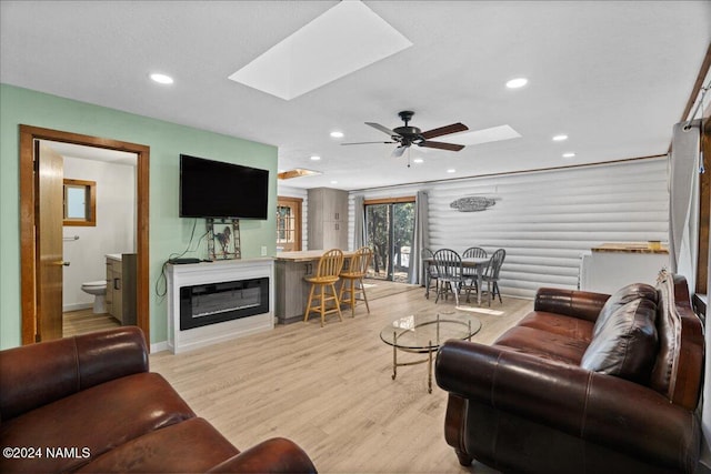 living room with a skylight, ceiling fan, and light hardwood / wood-style flooring