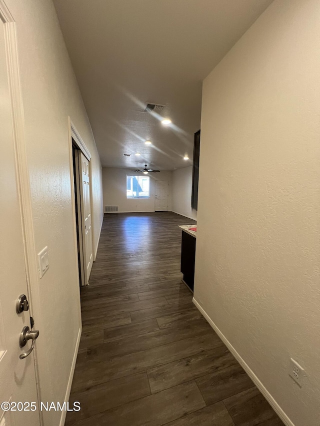 corridor featuring dark wood-style floors, visible vents, and baseboards