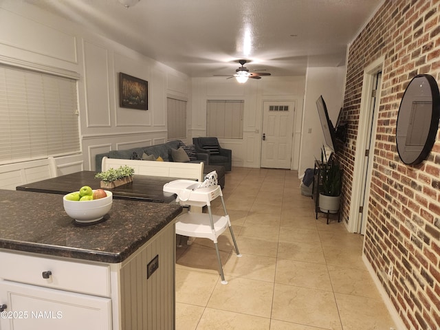 living area with light tile patterned floors, brick wall, ceiling fan, and a decorative wall