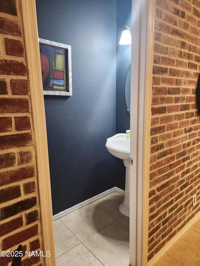 bathroom featuring brick wall, baseboards, and tile patterned flooring