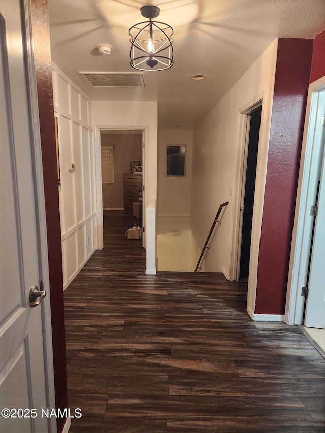 hall with dark wood-type flooring, visible vents, and an upstairs landing