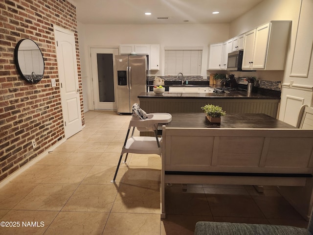 kitchen featuring dark countertops, brick wall, black range with gas stovetop, and stainless steel refrigerator with ice dispenser