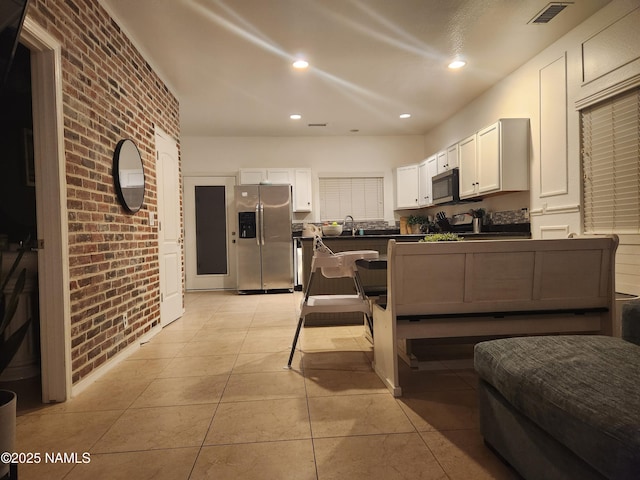 kitchen with dark countertops, visible vents, white cabinetry, brick wall, and stainless steel fridge with ice dispenser