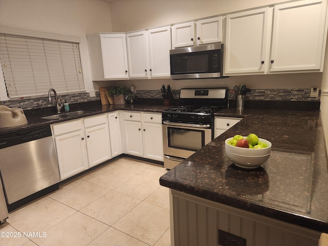 kitchen featuring white cabinets, decorative backsplash, dark stone countertops, stainless steel appliances, and a sink