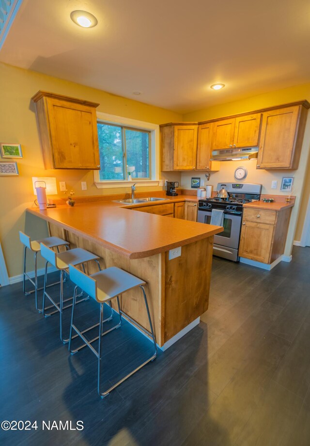 kitchen with dark wood-type flooring, sink, kitchen peninsula, stainless steel gas range oven, and a breakfast bar area