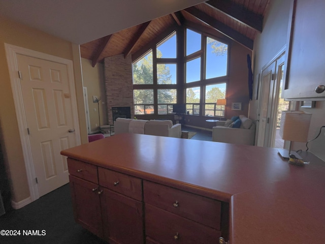 kitchen with beam ceiling, high vaulted ceiling, a stone fireplace, and wood ceiling