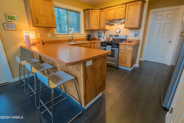 kitchen featuring a kitchen bar, sink, kitchen peninsula, stainless steel gas range oven, and dark hardwood / wood-style floors