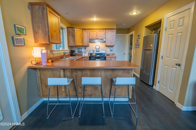 kitchen with kitchen peninsula, a kitchen breakfast bar, appliances with stainless steel finishes, sink, and dark hardwood / wood-style floors