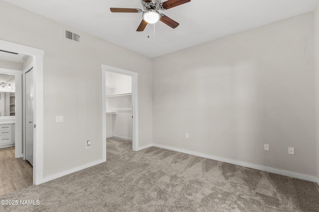 unfurnished bedroom with light carpet, a closet, a spacious closet, and ceiling fan