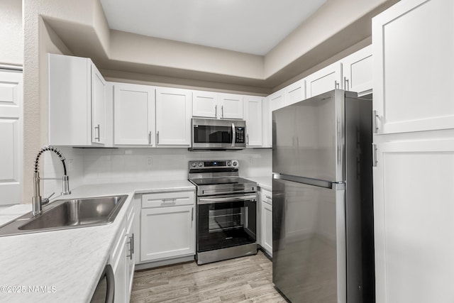 kitchen with white cabinets, sink, light hardwood / wood-style flooring, backsplash, and stainless steel appliances