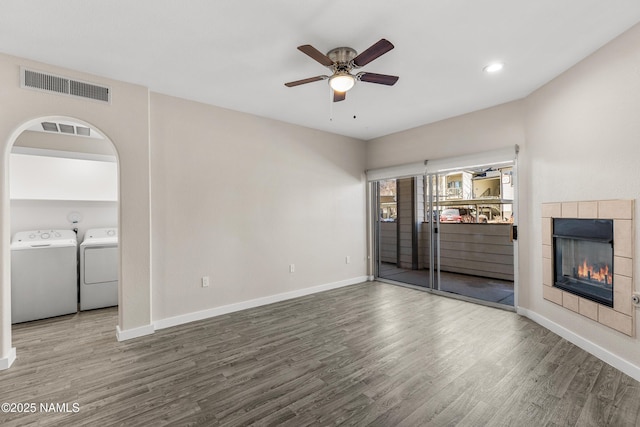 unfurnished living room featuring wood-type flooring, a tile fireplace, washing machine and dryer, and ceiling fan