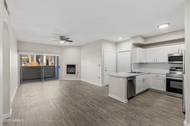 kitchen featuring wood-type flooring, white cabinetry, a tile fireplace, sink, and stainless steel appliances