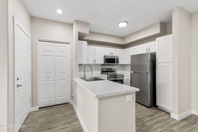 kitchen featuring appliances with stainless steel finishes, tasteful backsplash, white cabinetry, sink, and light wood-type flooring