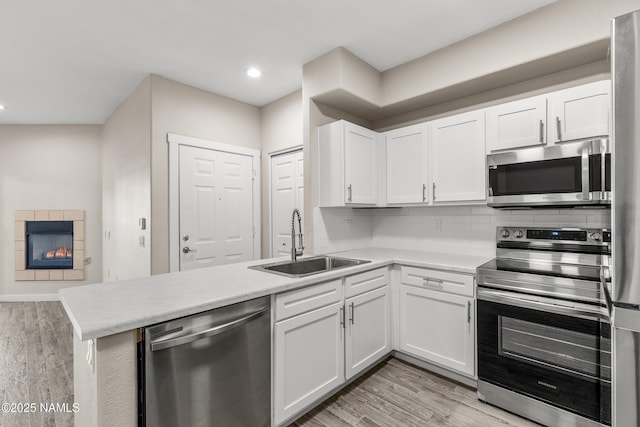 kitchen with kitchen peninsula, sink, white cabinets, light wood-type flooring, and stainless steel appliances