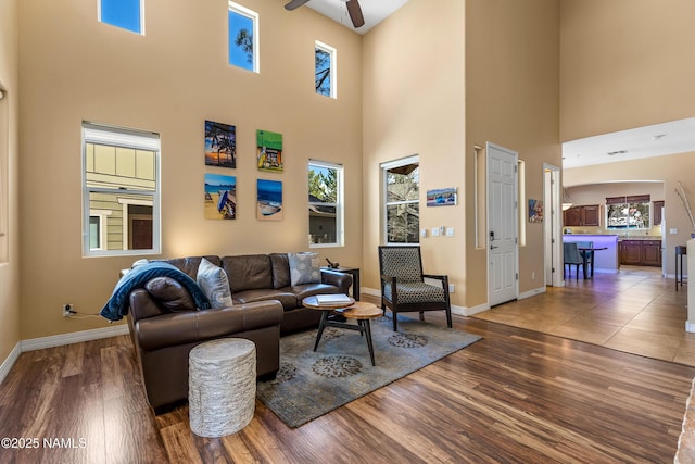 living area featuring wood finished floors, baseboards, a high ceiling, and ceiling fan