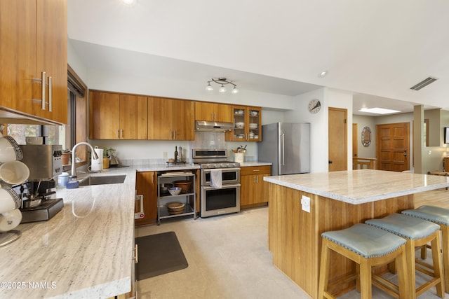 2169 E Skyline Dr, Flagstaff, AZ 86004 - kitchen featuring stainless steel appliances, brown cabinetry, a breakfast bar, glass insert cabinets, and a center island