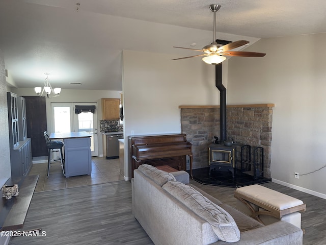 living room featuring vaulted ceiling, a wood stove, light wood-style flooring, baseboards, and ceiling fan with notable chandelier