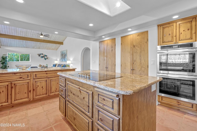 kitchen featuring light stone countertops, a center island, double oven, vaulted ceiling with beams, and black electric cooktop