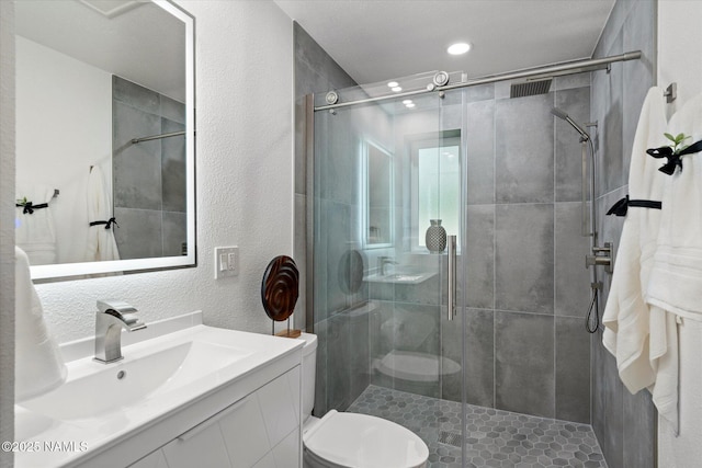 bathroom with toilet, a textured wall, a stall shower, vanity, and recessed lighting