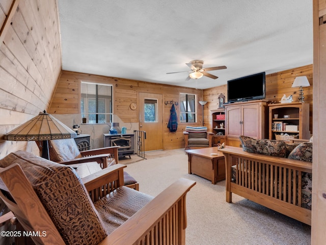 7284 N Buck Ridge Rd, Williams, AZ 86046 - living area featuring a wood stove, wood walls, a ceiling fan, light carpet, and a textured ceiling