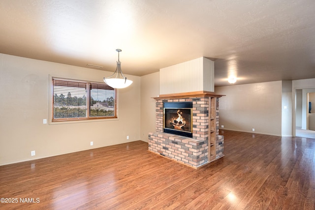 unfurnished living room featuring a brick fireplace, visible vents, baseboards, and wood finished floors