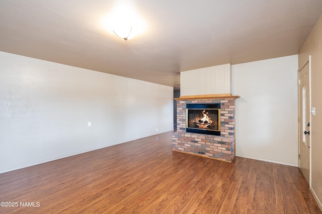 unfurnished living room featuring a brick fireplace, baseboards, and wood finished floors