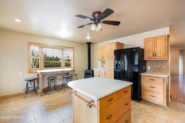 kitchen featuring decorative backsplash, a center island, a wood stove, black refrigerator with ice dispenser, and light countertops