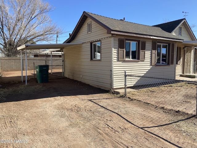 view of side of home with concrete driveway, a carport, roof with shingles, and fence