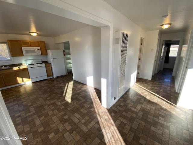 kitchen with brick floor, a heating unit, a sink, white appliances, and baseboards