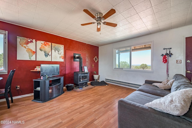 living room with ceiling fan, baseboard heating, a wood stove, and light hardwood / wood-style flooring