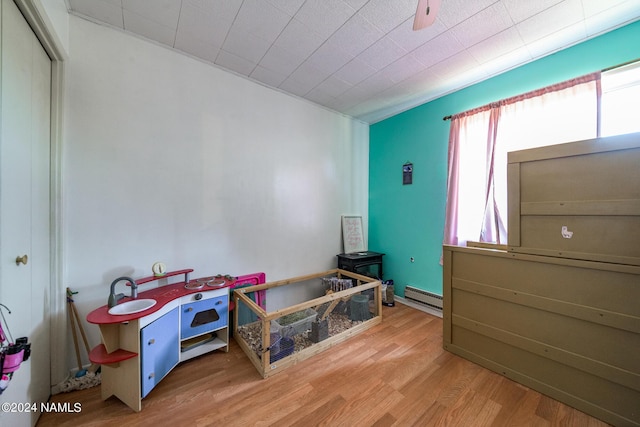 game room featuring wood-type flooring, baseboard heating, and ceiling fan