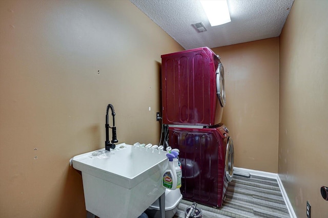 laundry room featuring stacked washing maching and dryer, hardwood / wood-style flooring, and a textured ceiling