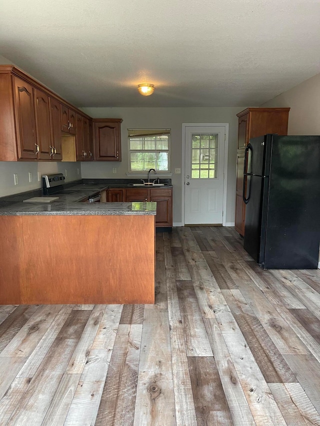 kitchen featuring black fridge, stainless steel electric stove, kitchen peninsula, sink, and light hardwood / wood-style floors