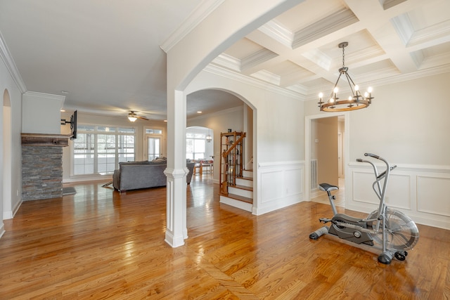 workout room featuring crown molding, coffered ceiling, ceiling fan with notable chandelier, and light hardwood / wood-style floors