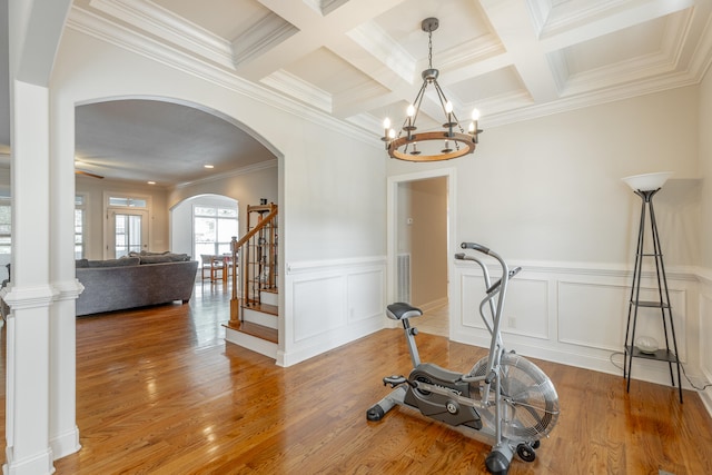 workout area with crown molding, coffered ceiling, hardwood / wood-style floors, and ceiling fan with notable chandelier